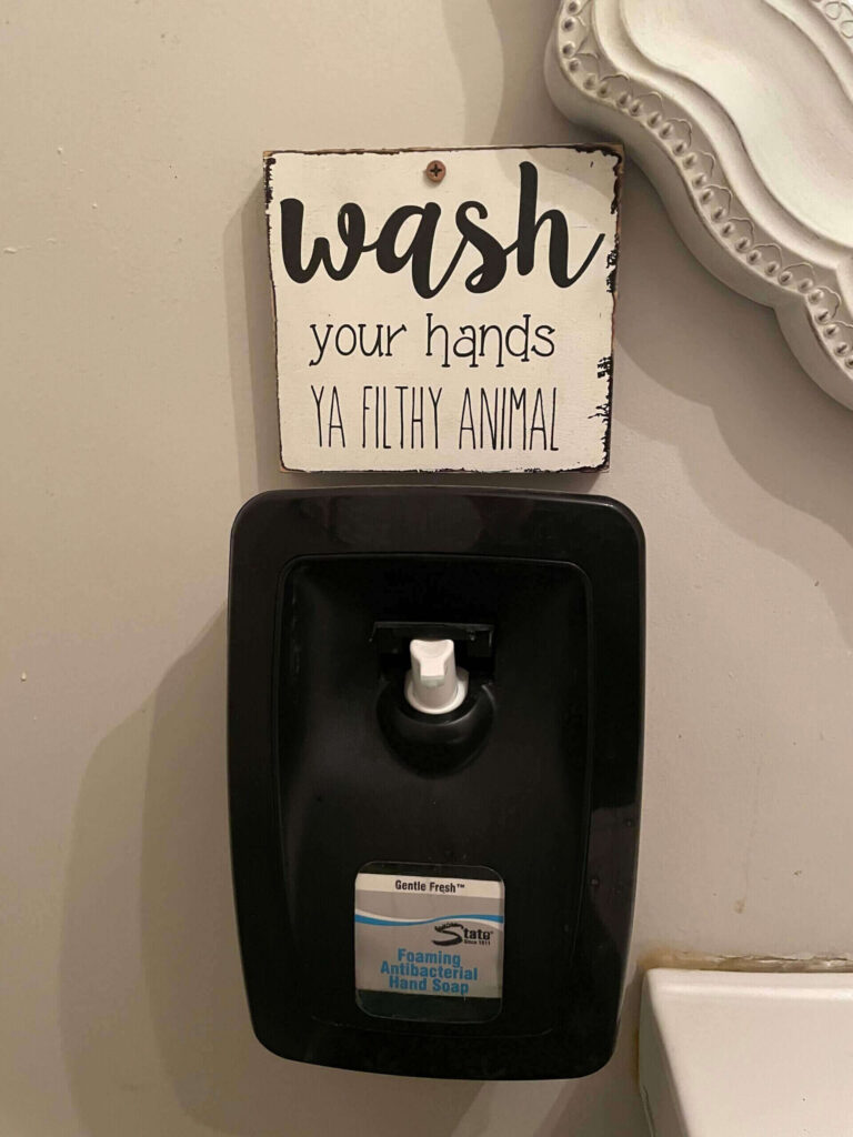 Bathroom soap dispenser with sign saying "wash your hands ya filthy animal."