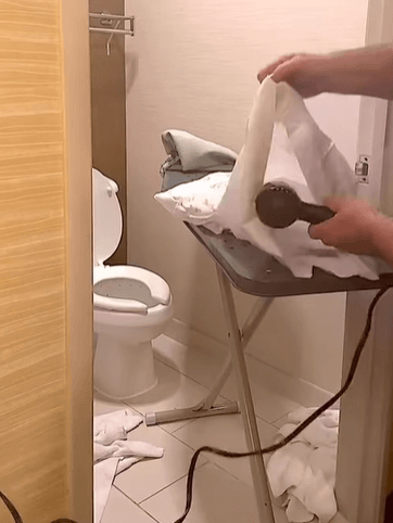 a hair dryer being placed inside a pillow case on an ironing board in a bathroom